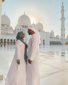 a man and woman standing in front of a large white building with many arches on it