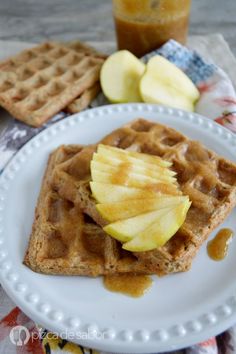 two waffles on a plate with apple slices and caramel syrup next to them