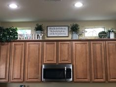 a kitchen with wooden cabinets and plants on the top shelf above the microwave, is shown in this image