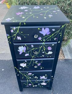 a black dresser with purple flowers painted on the front and sides, along with green leaves