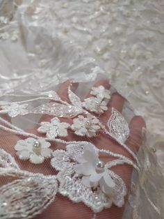 someone is holding something in their hand with white lace on it and flowers all over the fabric