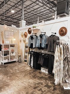 a clothing store with clothes on racks and hats hanging from the ceiling, in front of an open area