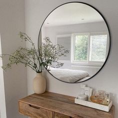 a round mirror hanging on the wall above a wooden dresser with a plant in it