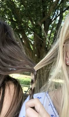 two women with long hair blow drying their hair in front of a tree and another woman holding her hair