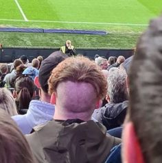 a crowd of people sitting in front of a soccer field with a man standing on the sidelines