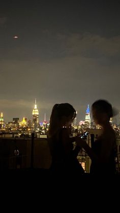 two people looking at their cell phones in front of the city lights and skyscrapers