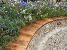 a garden filled with lots of flowers next to a stone wall and wooden steps leading up to it