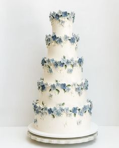 a three tiered white cake with blue flowers on the top and bottom, sitting on a platter