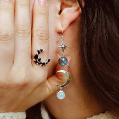 Stunning and sparkly celestial dangly earrings for boho women. These sterling silver earrings feature labradorite and Moonstone gemstones with celestial imagery including a star, planet Saturn and a crescent moon. Labradorite is commonly known as the stone of things ‘unseen.’ It provides energetic and spiritual protection while also warding off negative vibes. Moonstone delicately connects us to the wisdom of the moon and our own inner goddess. It is also deeply connected to water. Material: Gen Celestial Silver Labradorite Jewelry, Silver Labradorite Jewelry With Moon Charm, Celestial Moonstone Jewelry With Sun And Moon Design, Celestial Sun And Moon Moonstone Jewelry, Silver Sun And Moon Drop Earrings, Moonstone Earrings With Moon Charm, Silver Sun And Moon Design Drop Earrings, Silver Spiritual Moon Phase Earrings, Celestial Sterling Silver Earrings