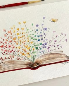 an open book painted with watercolors on white paper next to a red pencil