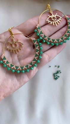 a hand holding a pair of green beaded hoop earrings with gold accents on it