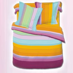 a bed with colorful striped sheets and pillow cases on top of each other, in front of a pink wall