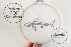 someone is holding up a embroidery project with an image of a shark in the middle