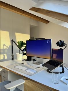 a desk with a laptop, monitor and camera on it in front of a window