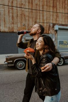 a man and woman standing next to each other while holding pizza in front of them