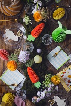 an arrangement of colorful paper flowers and napkins on a wooden table with place settings