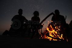 three people sitting around a campfire at night