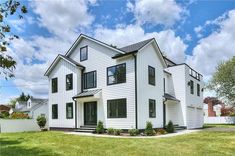 a white two story house with black windows and green grass in front of the house