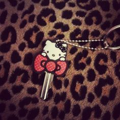 a hello kitty keychain with a red bow on it's head sitting on a leopard print surface