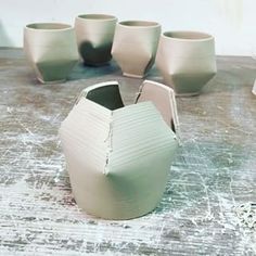 several white vases sitting on top of a wooden table next to cups and spoons