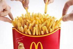 two hands reaching for french fries in a mcdonald's bucket