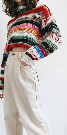 a woman in white pants and a multicolored sweater is posing for the camera