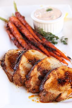 grilled chicken and carrots on a white plate with dipping sauce in the background