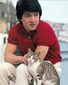 a man sitting on top of a rock next to a gray and white cat in his lap