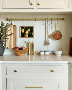 a kitchen with white cabinets and gold handles on the countertop, pots and pans hanging from hooks