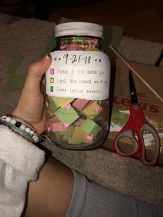 a person is holding a jar full of crafting material and scissors on the floor