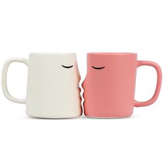 two coffee mugs with faces drawn on them, one pink and the other white