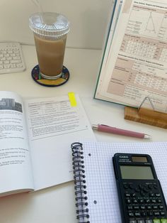 an open book, calculator and pen on a desk next to a cup of coffee