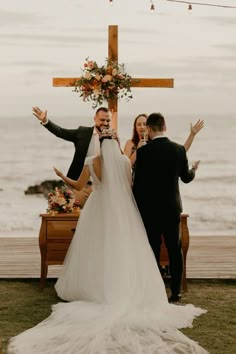 a bride and groom standing in front of a cross with their hands up at the alter