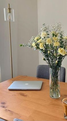 a wooden table topped with a laptop computer next to a vase filled with yellow flowers