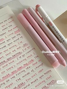 three pink pens sitting next to each other on top of a notepad with writing