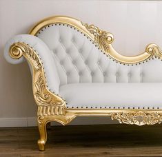 a white and gold couch sitting on top of a hard wood floor next to a wall