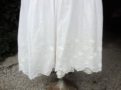 "This is a white cotton petticoat from 1890's to 1905. It features a bustle back with gathering in the rear. There is a slight train with the longer back. This petticoat has a double layer at the hem. The top flounce is embroidered with pretty little flowers and leaves and a scalloped edge. The underlayer has a lace edged flounce. There is a band of insertion lace at the top of the top flounce to run a ribbon. This petticoat closes with a mother-of-pearl button. There are 2 pinhead size faint sp Regency Style White Petticoat For Daywear, White Regency Style Petticoat For Daywear, Edwardian Petticoat Pattern, White Regency Style Cotton Petticoat, White Cotton Petticoat With Lace Trim, Vintage Spring Petticoat With Lace Trim, Edwardian Underclothes, Victorian White Cotton Petticoat, Insertion Lace