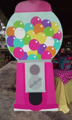 a pink and white machine with lots of balloons on it's front end, next to a table