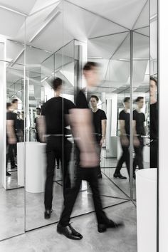 a group of people standing in front of a mirrored wall with one person walking by