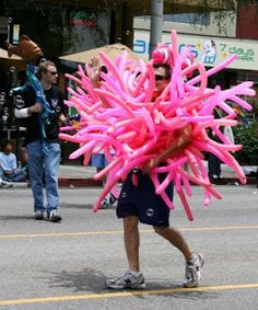 a man is walking down the street with pink balloons on his head