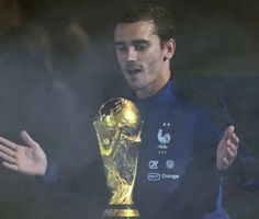 a man holding a soccer ball in his hand while standing next to a golden trophy