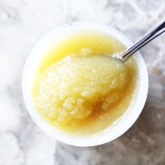 a cup filled with yellow liquid on top of a marble countertop next to a spoon