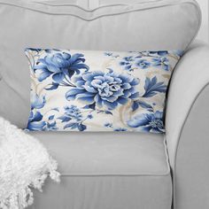 a blue and white flowered pillow sitting on top of a gray couch next to a white blanket