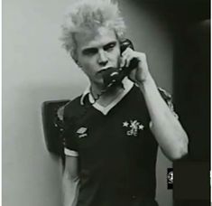 a man with blonde hair talking on a cell phone while standing in front of a mirror