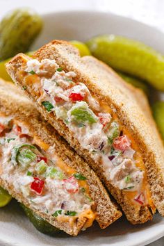 a sandwich cut in half sitting on top of a white plate next to pickles