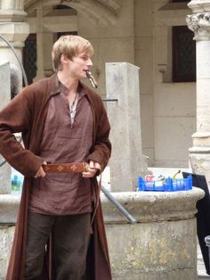 a man dressed in medieval clothing standing next to a fountain with a pipe sticking out of it's mouth