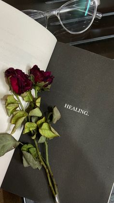 a rose laying on top of an open book with reading glasses in front of it