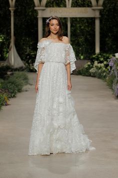 a model walks down the runway in an off - shoulder wedding dress with ruffled sleeves