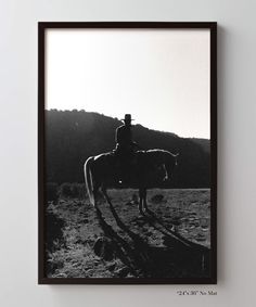 a black and white photo of a man on a horse in the desert with mountains in the background