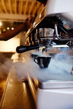 a coffee machine with steam coming out of it's top and the espresso being poured into its cup